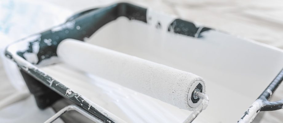 Close-up of a paint roller in a paint tray on a clean drop cloth, indicating preparation for painting.